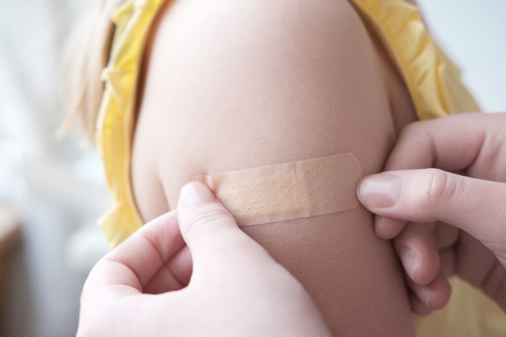 Woman hands putting adhesive bandage on child's hand